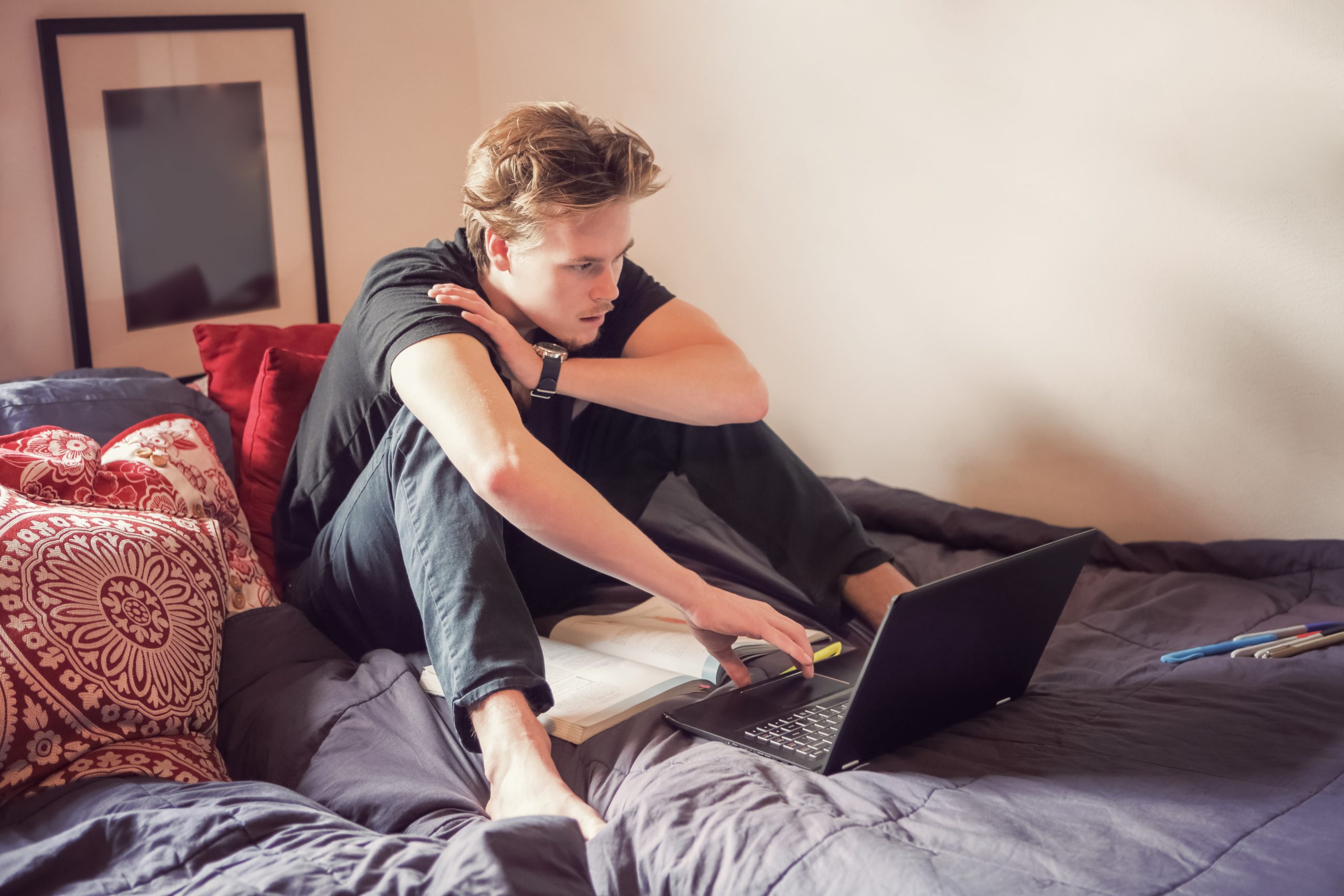 A high school student studies on a laptop in his bedroom