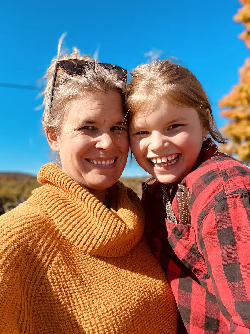 A photograph of VTVLC Interim Director, Ashley Newton, outside surrounded by mountains and trees with her daughter, Quinn.