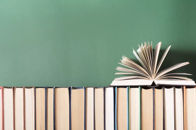 A row of books arranged in front of a chalkboard, with an open book atop the row.