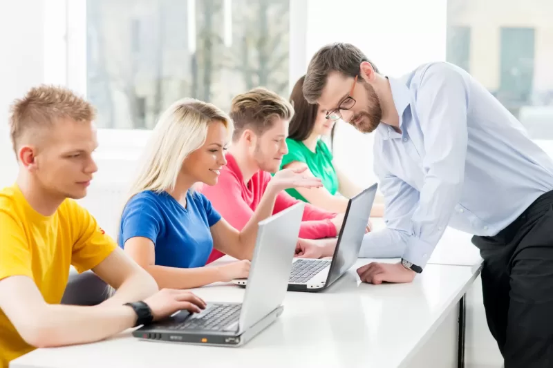 Photograph showing a teacher assisting students in a computer lab