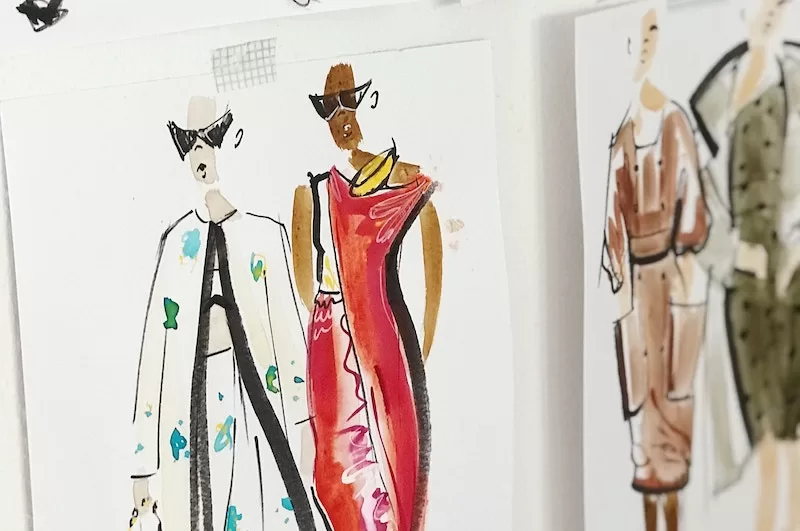 Photograph showing fashion design drawings taped to a bulletin board.