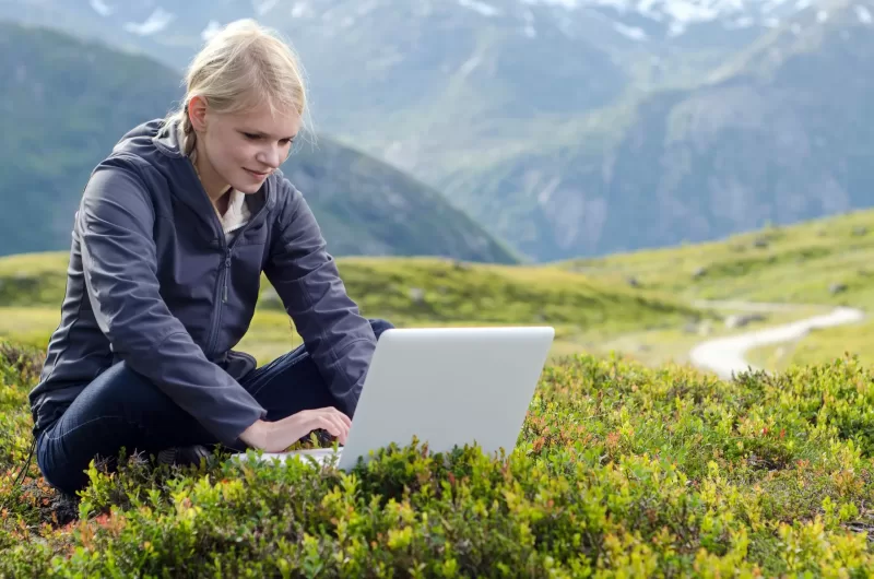 Student works on a laptop in a mountainous landscape.