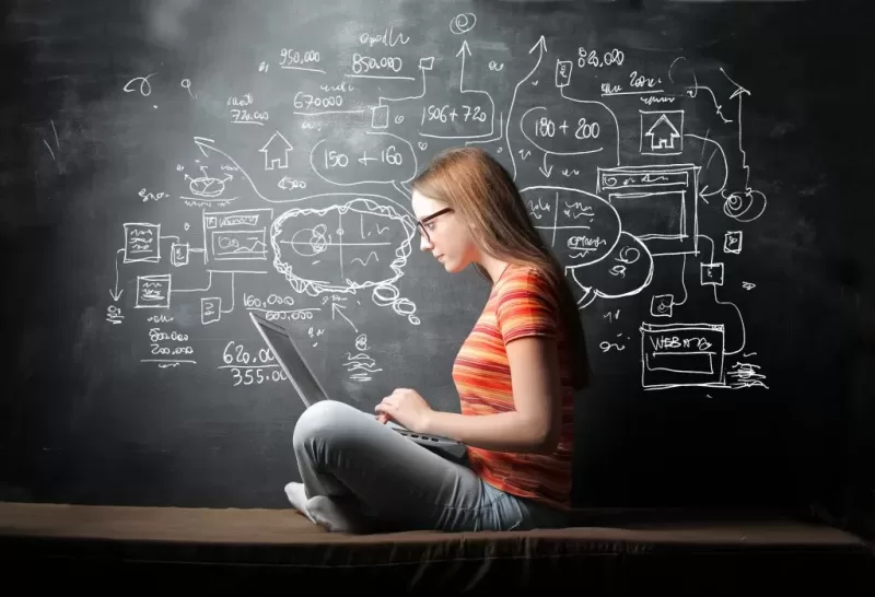 Image depicting a student operating a laptop in front of a blackboard where a mindmap or brainstorming chart has been drawn.