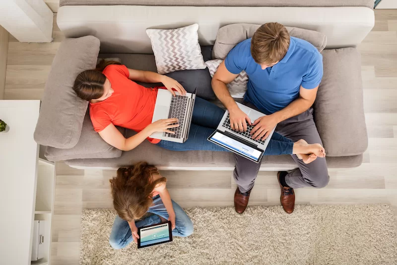 Image depicting a family working on laptops and tablets in a living room.