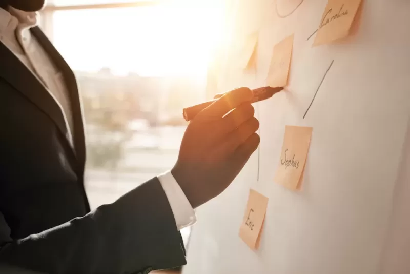 Image depicting a professional taking part in a brainstorming activity involving sticky notes pinned to a wall as part of a chart.