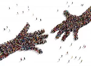 Image depicting birds-eye view of a crowds of people forming the shape of two hands reaching for one another, symobolizing collaboration, partnership, or connection.