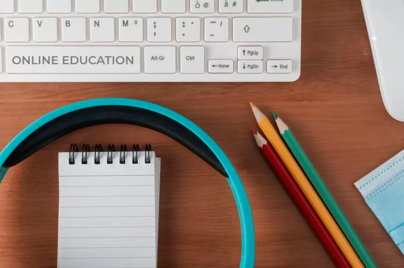 Photograph of a desk, containing a keyboard, computer mouse, stenographer's pad, headphones, and pencils.