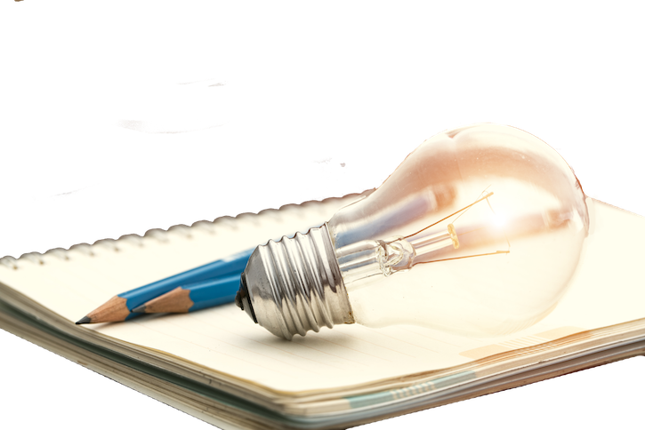 A photograph of an illuminated lightbulb and pencils on top of a notebook, symbolozing idea generation.