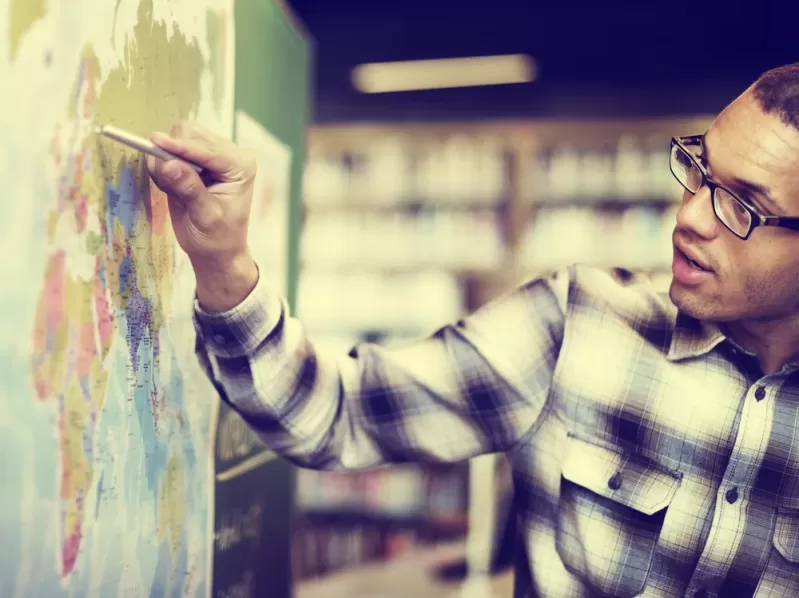 Photograph showing a student locating a point on a world map with a pen.