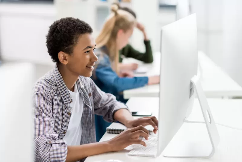 Image depicting a student smiling and utilizing a computer in a computer lab.