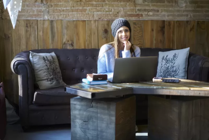 Image depicting a student working on a laptop from a cozy setting.