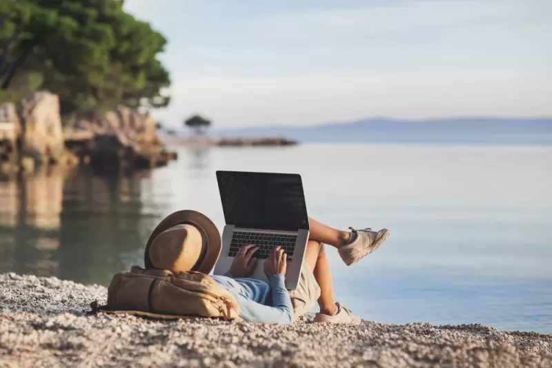 Student works on laptop from a beachfront.