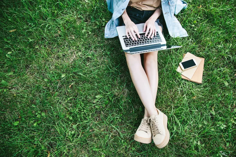 Student works on a laptop outside on a lawn.